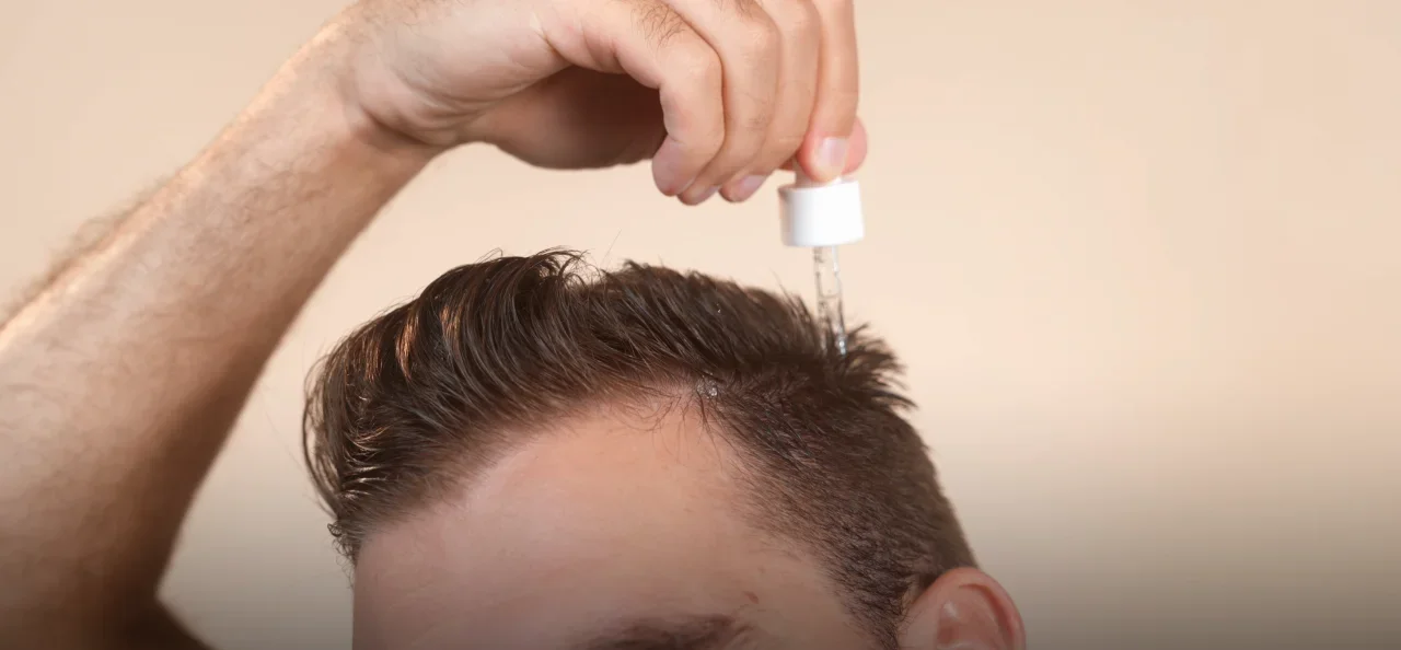 Man applying hair serum to scalp using a dropper on short hair.